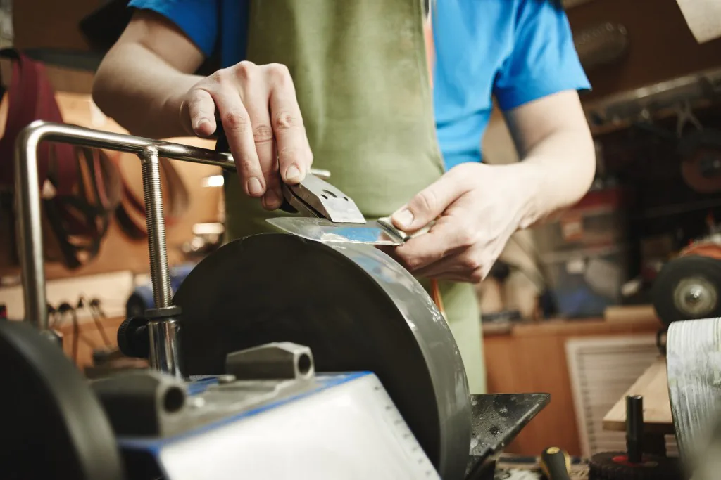 Technician sharpening a knife on a grinding wheel in a workshop